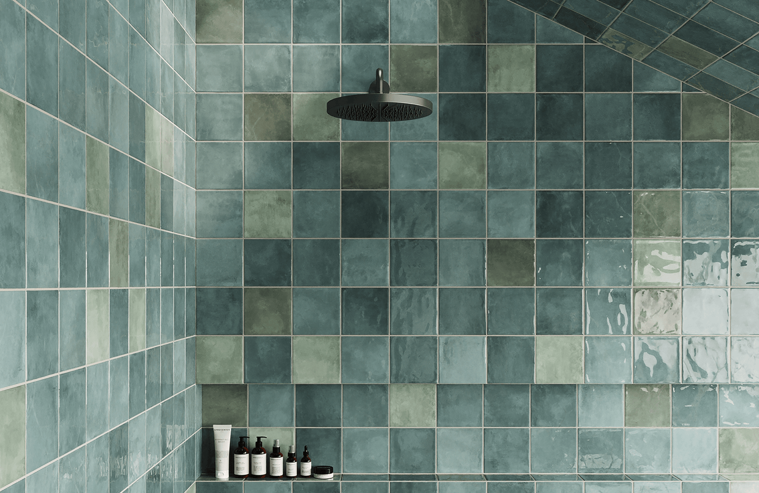 Elegant shower space with glossy, handcrafted green bathroom tiles in varied shades, featuring a sleek black rainfall showerhead.
