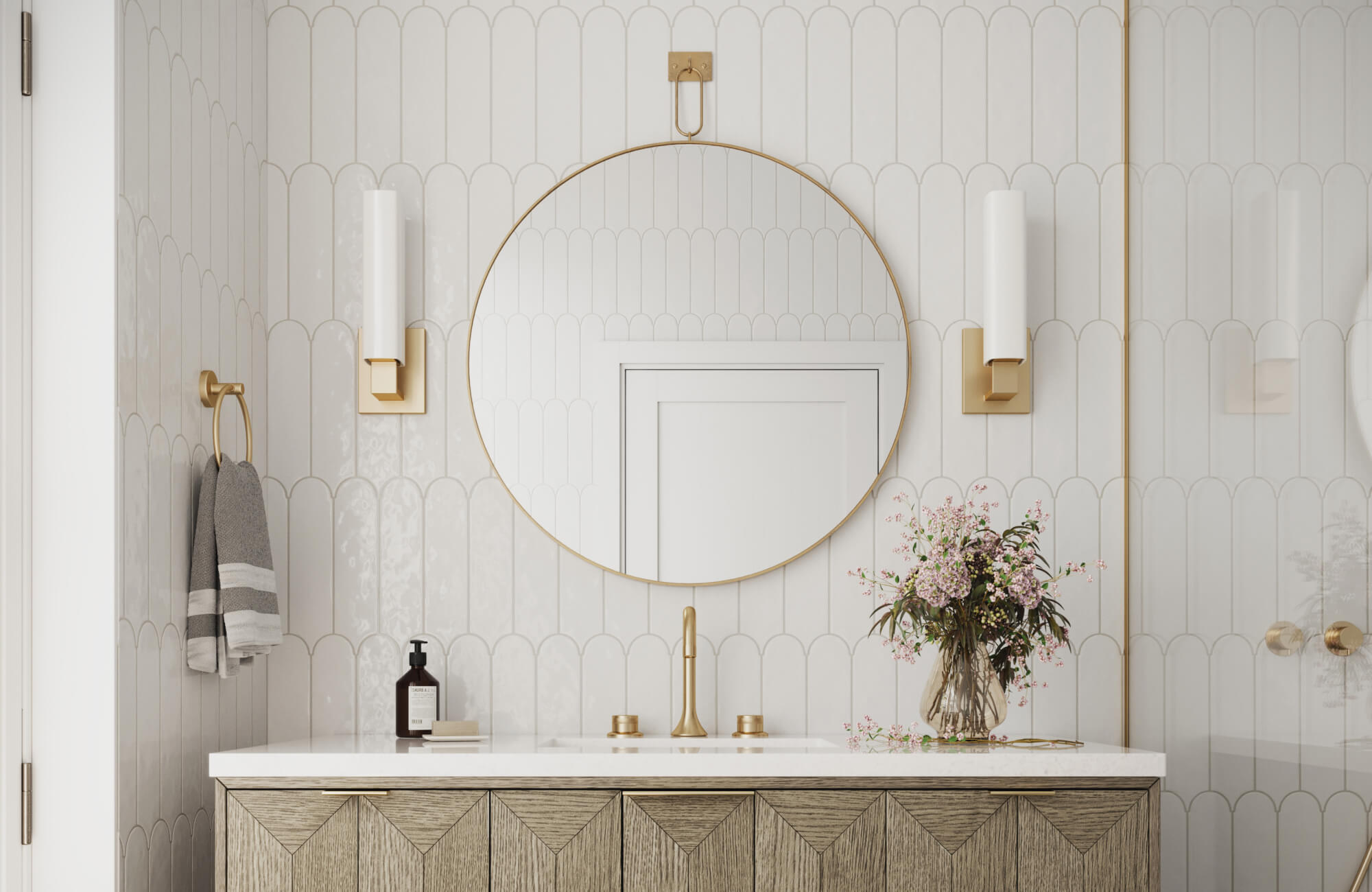 Elegant bathroom featuring a circular mirror, brushed brass accents, fluted white sconces, and a floral arrangement on a chevron-patterned vanity.