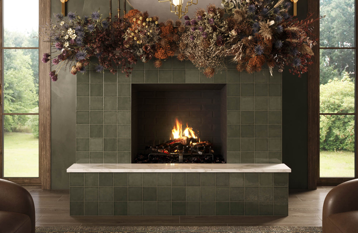 A modern tiled fireplace in deep olive green with a marble hearth, framed by large windows and topped with an abundant dried floral arrangement.