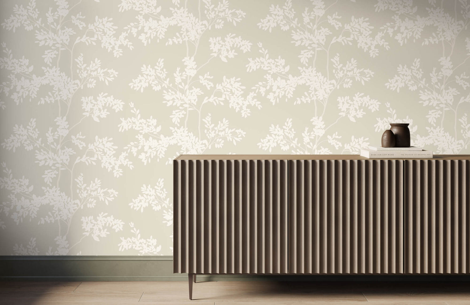 A beige fluted sideboard topped with a dark brown clay vase and stacked books sits against a soft beige wallpaper with a white botanical branch pattern.