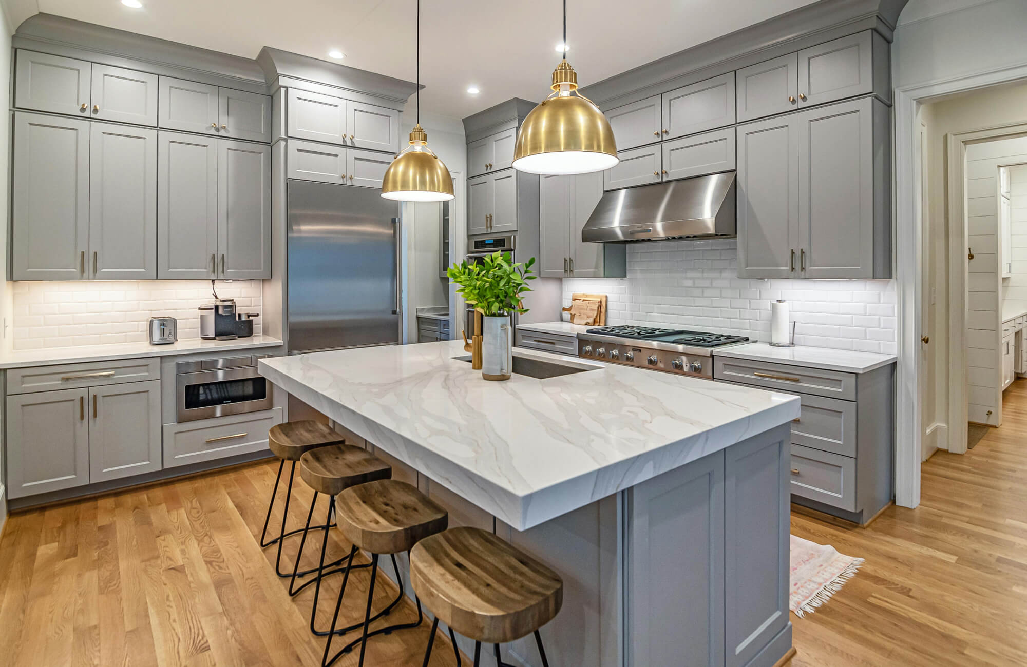 Modern kitchen with a large island topped in white stone, styled with brass pendant lights that add warmth and visual focus without changing the cabinetry layout.