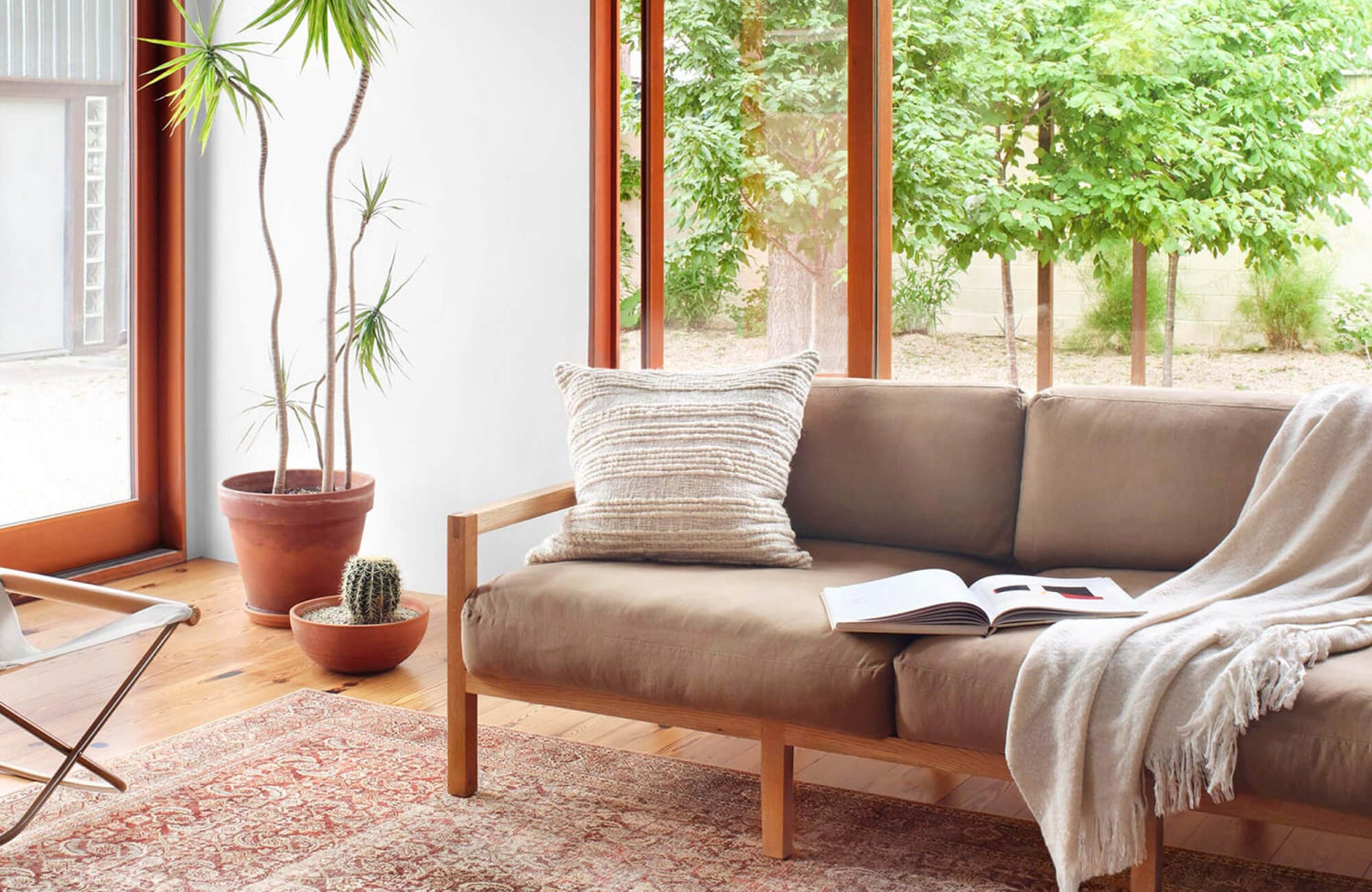 Cream textured throw pillow resting on a minimalist sofa beside large windows with a burgundy/khaki rug.