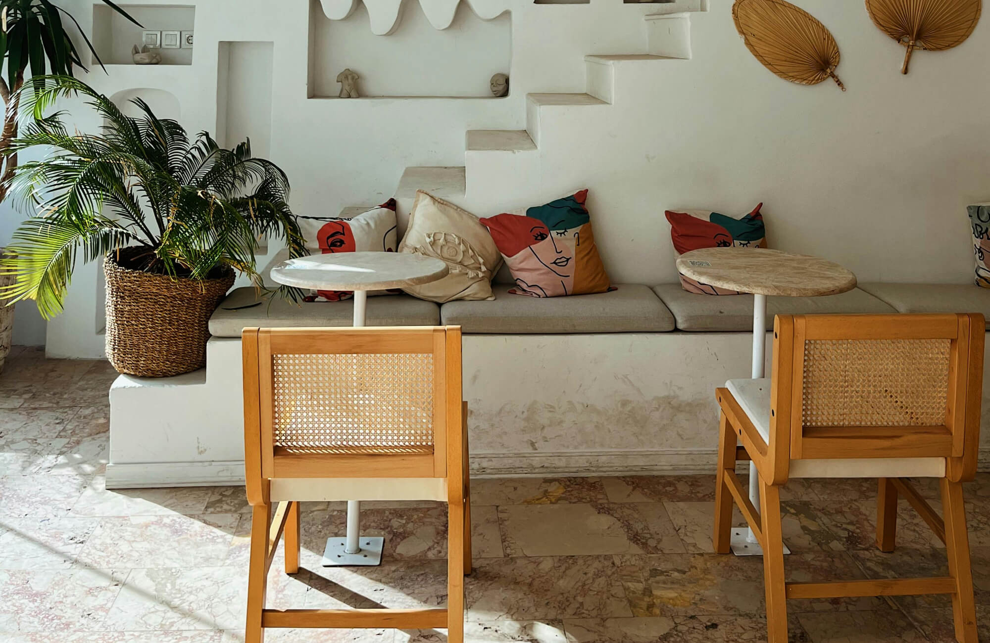 Warm-toned travertine floor tiles run beneath the built-in bench and café-style seating, adding natural variation that complements the airy, sunwashed interior.