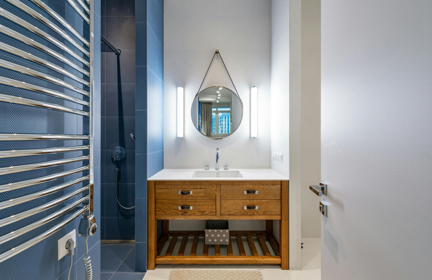Modern bathroom with a light wood vanity, white countertop, and open shelf design beneath a round mirror.