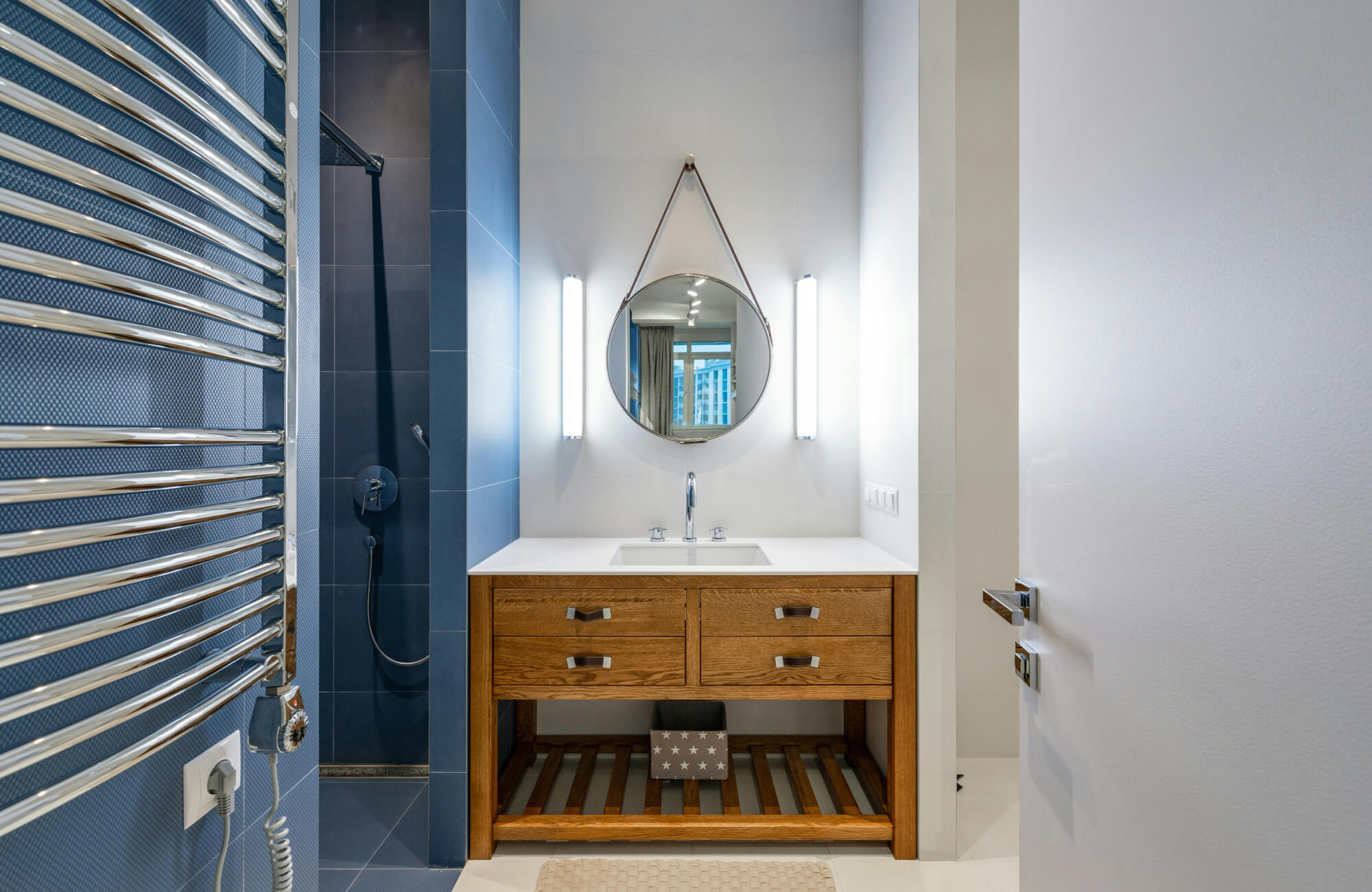 Modern bathroom with a light wood vanity, white countertop, and open shelf design beneath a round mirror.