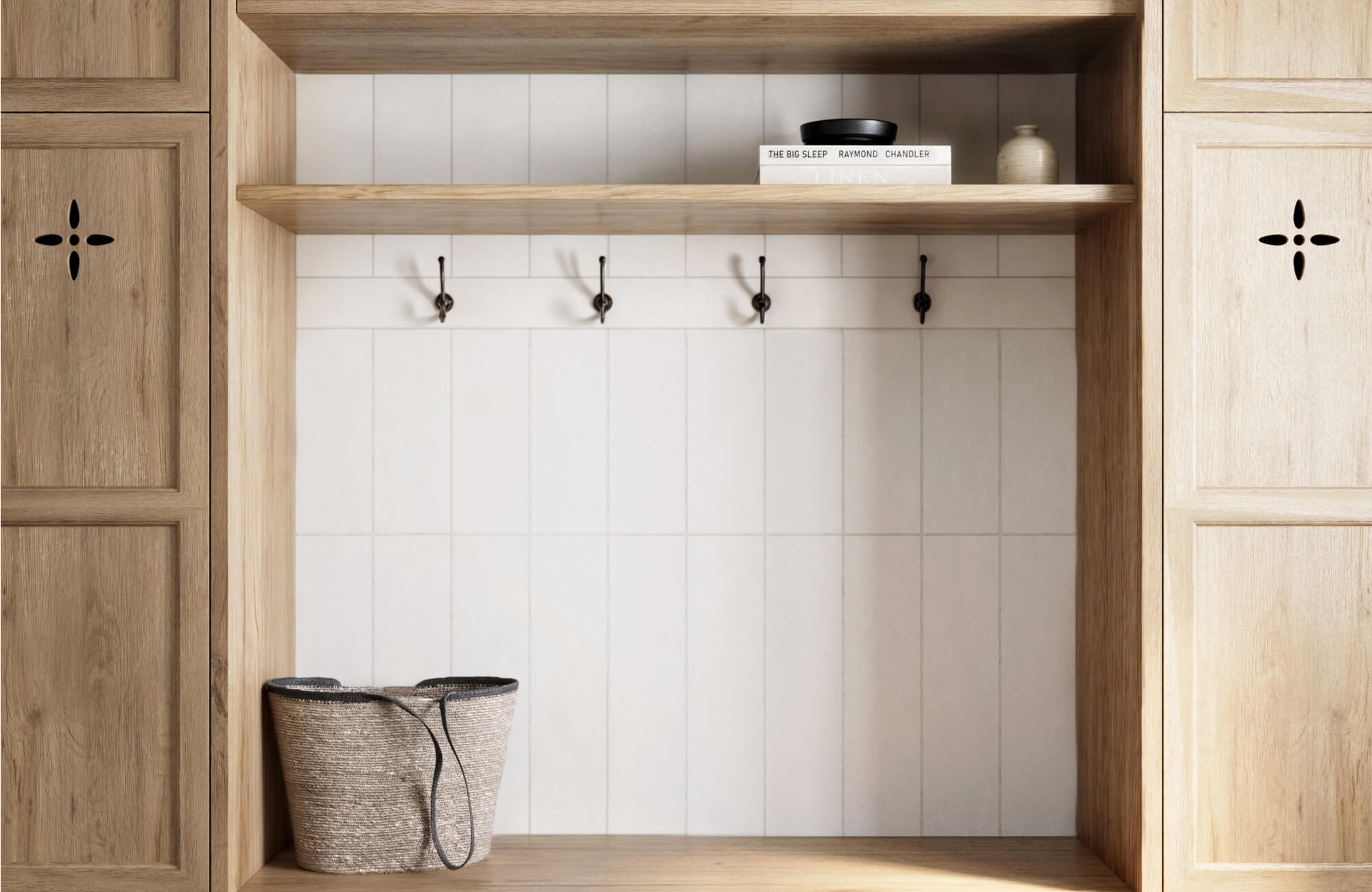 Light wood mudroom bench with vertical white subway tiles and black hooks, styled with books and a woven basket.