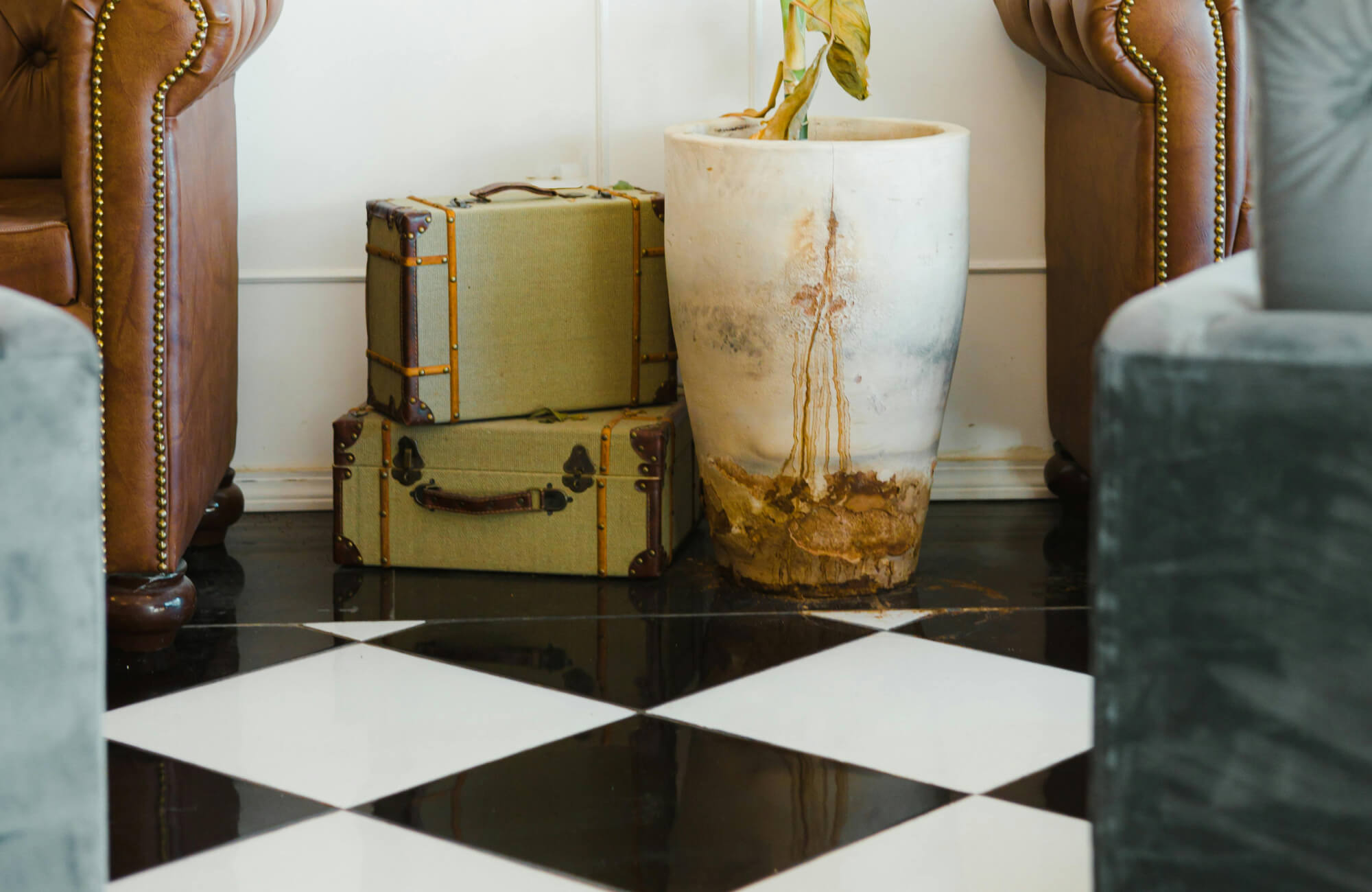 Black and white checkerboard tile flooring with vintage suitcases and a distressed ceramic planter in a cozy living space.