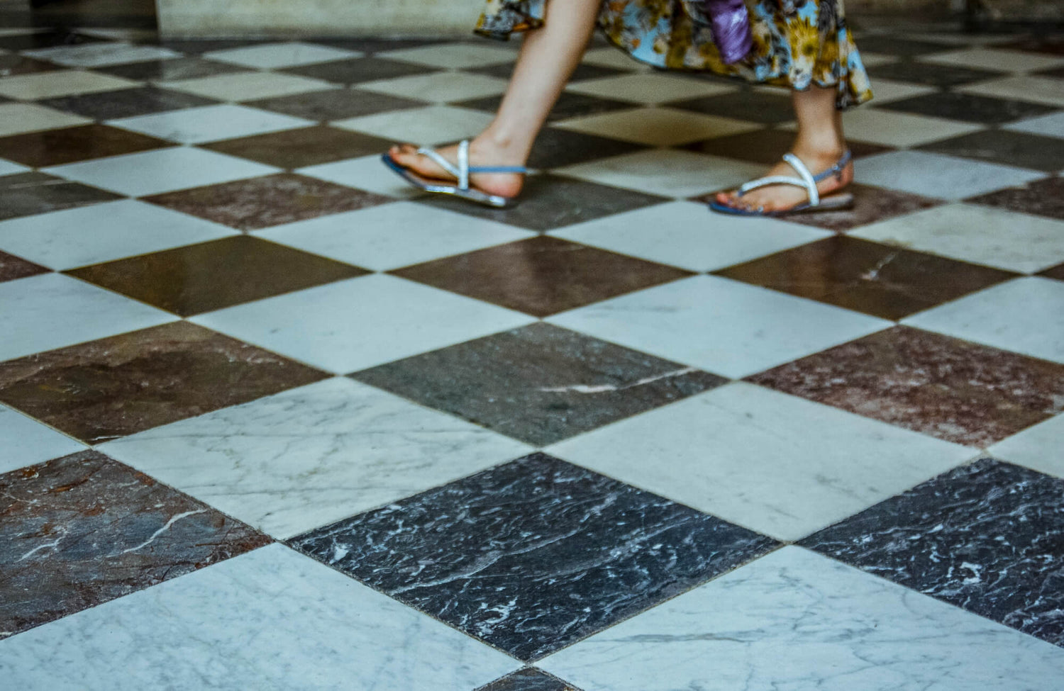 A woman in sandals walks across a classic checkerboard floor, highlighting the timeless elegance of the design.
