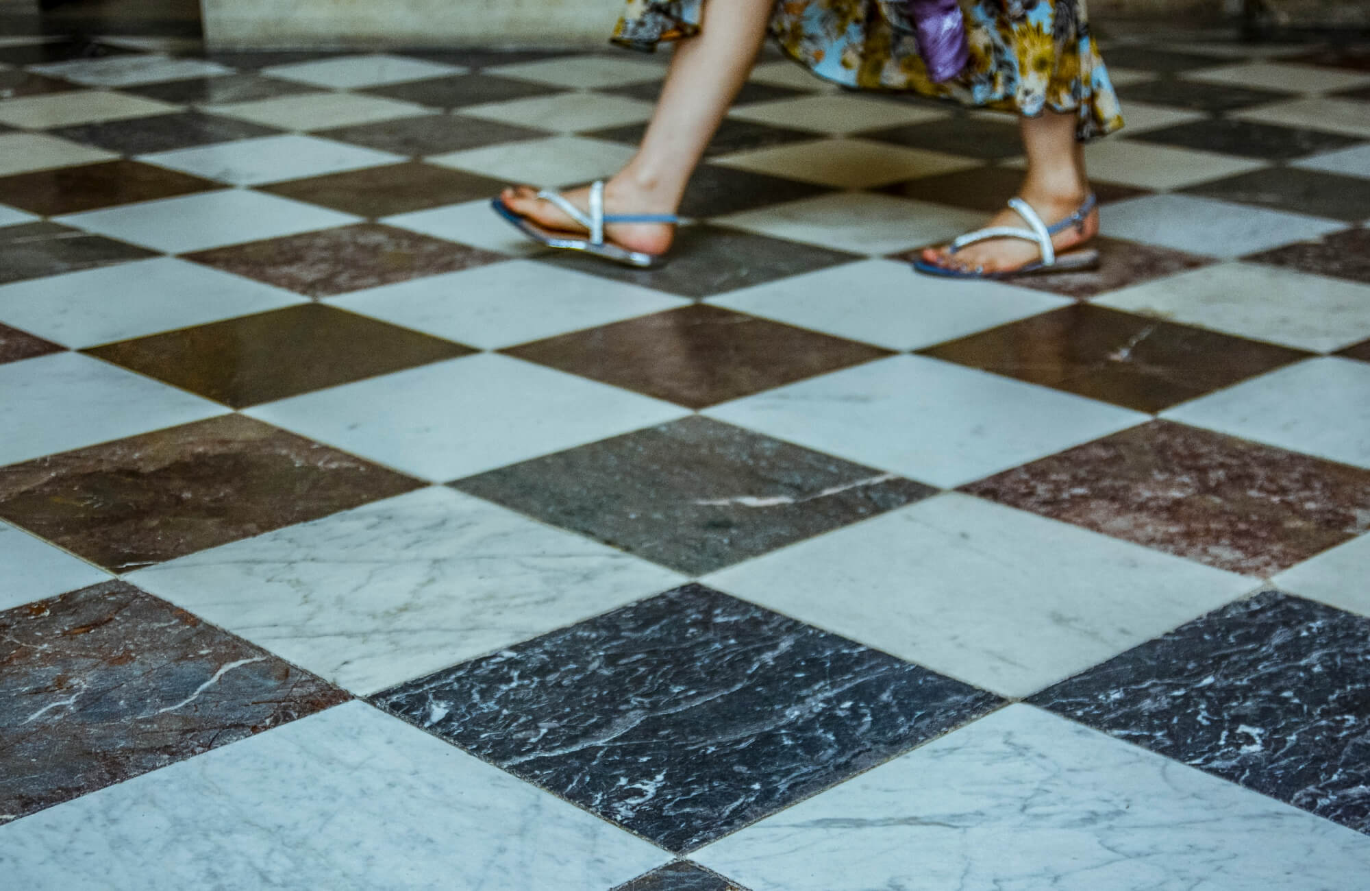 A woman in sandals walks across a classic checkerboard floor, highlighting the timeless elegance of the design.