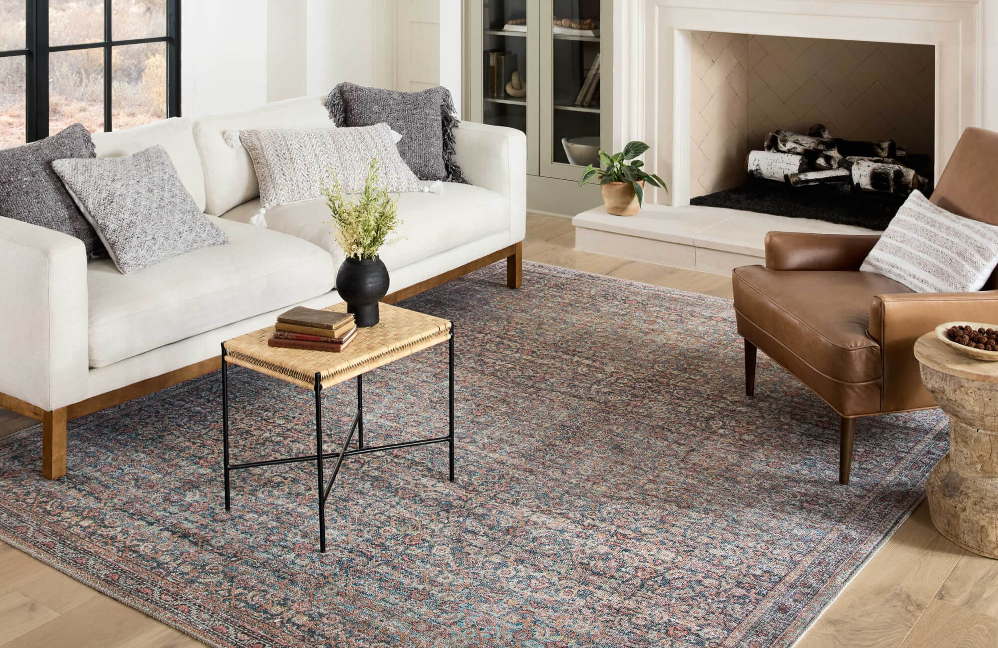 Cozy living room with a large vintage-style rug anchoring a cream sofa, leather armchair, and black-accented woven table