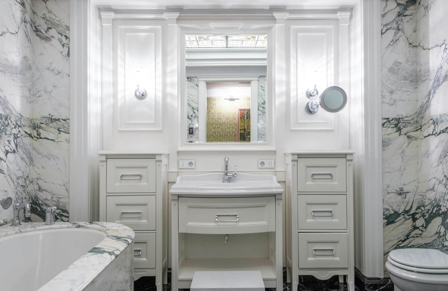 Luxurious bathroom with bold-veined white marble walls and bathtub surround paired with classic white cabinetry.
