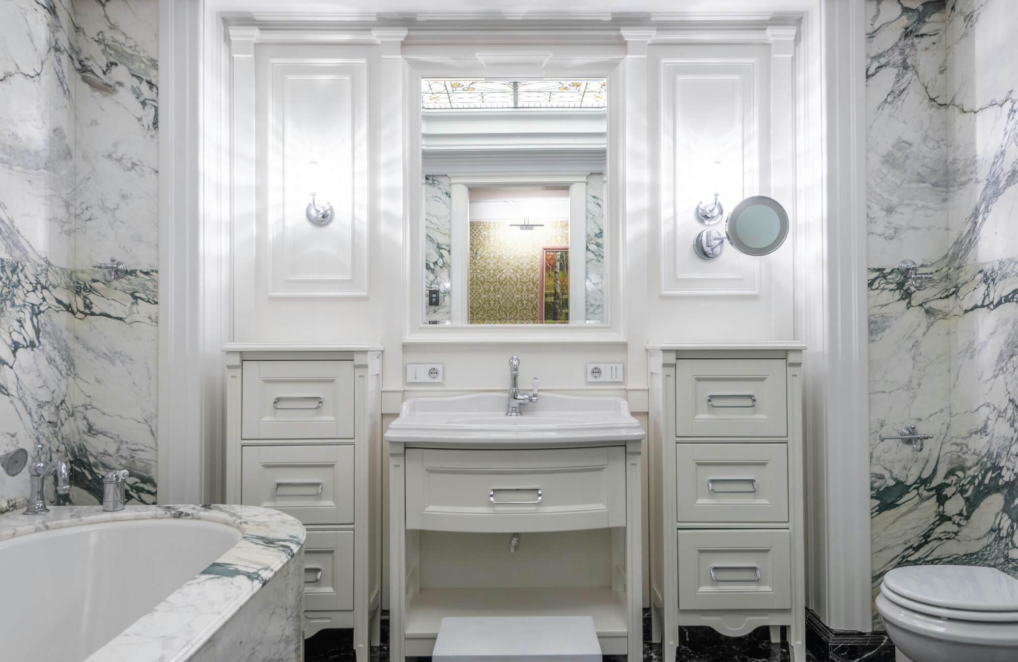 Luxurious bathroom with bold-veined white marble walls and bathtub surround paired with classic white cabinetry.
