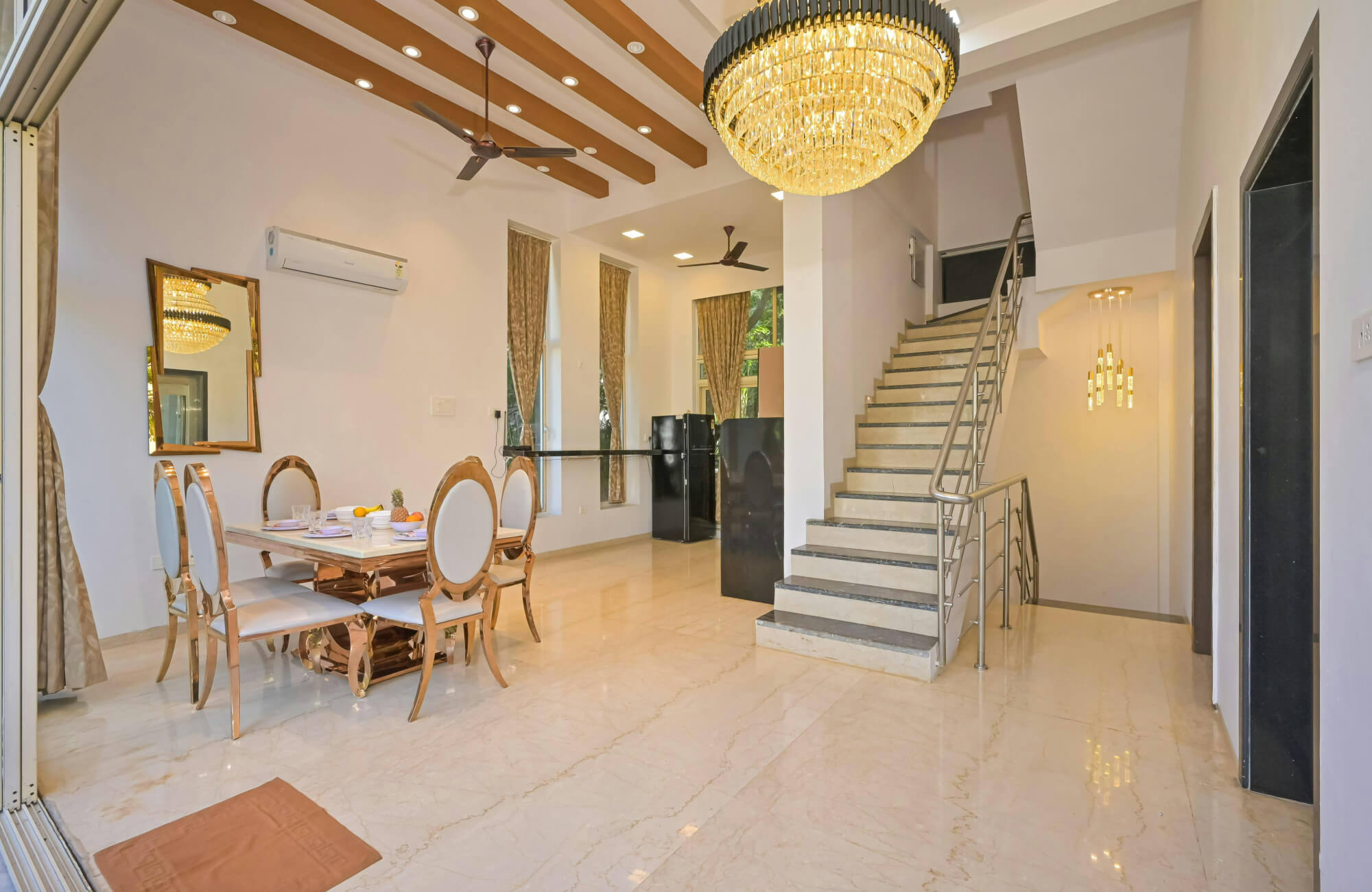 Luxurious beige marble flooring with subtle veining enhances this elegant dining and stair area with gold accents and chandeliers.