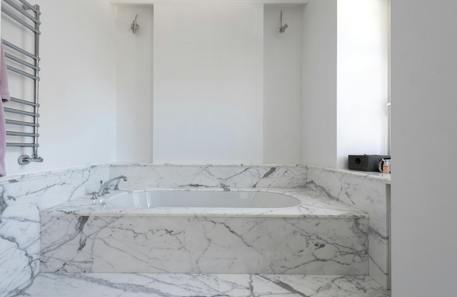 Built-in bathtub surrounded by white marble with gray veining in a minimalist modern bathroom interior.