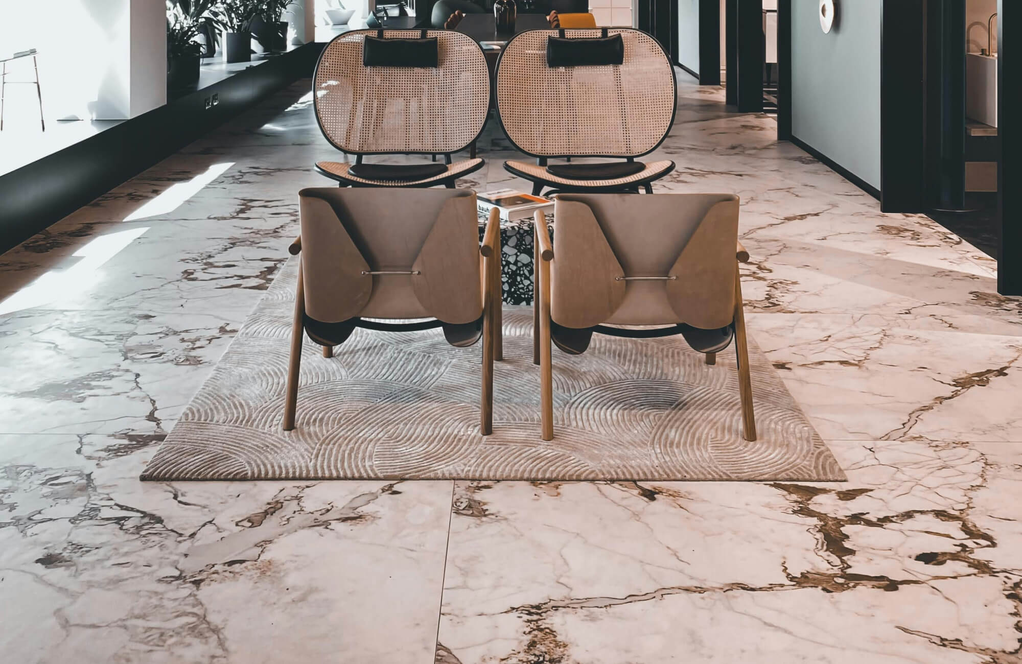 Modern lounge area with sleek, marble tile flooring and stylish wooden chairs on a textured rug.