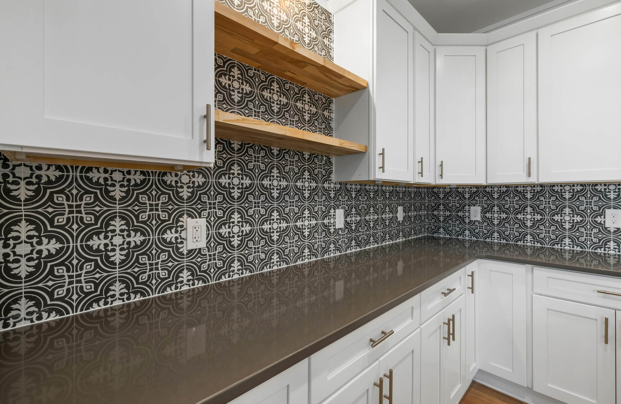 Kitchen with black and white Moroccan-pattern backsplash adding bold contrast against white cabinets and wood shelves.