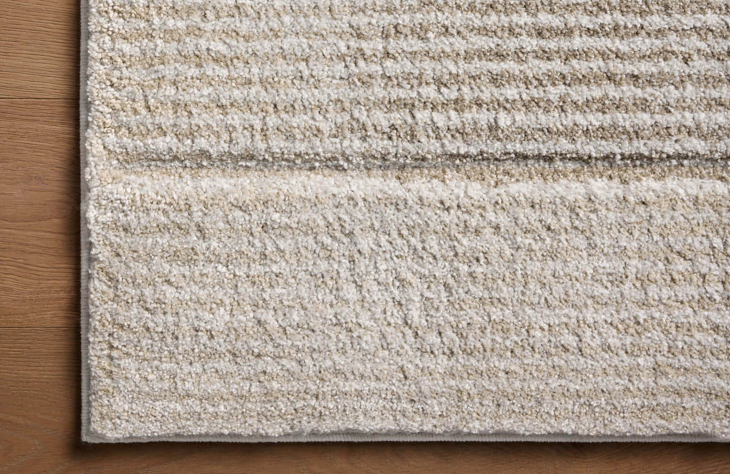 Close-up of a plush polypropylene rug with a soft, striped texture in neutral beige tones, laid over warm wood flooring.