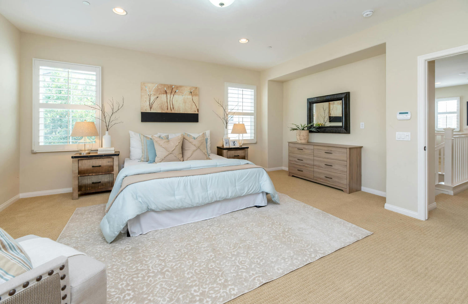 Bright and serene bedroom featuring a soft, patterned polypropylene rug layered over a beige area rug, complementing light wood furniture and pastel bedding.
