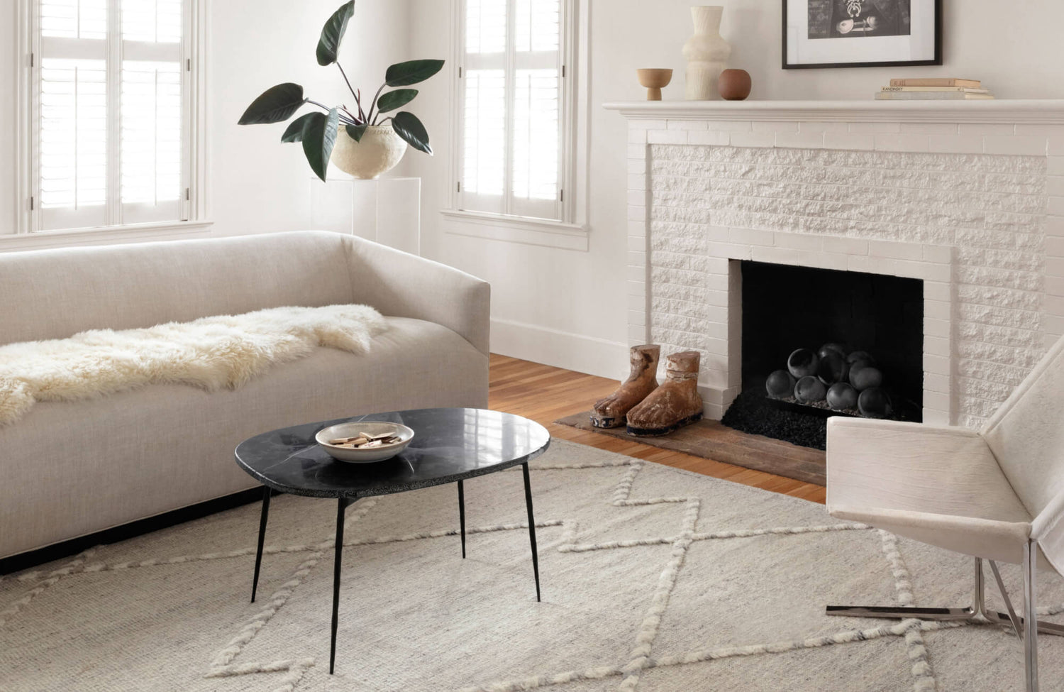 Modern minimalist living room with cream tones, featuring a textured wool rug, white brick fireplace, and sleek black coffee table.