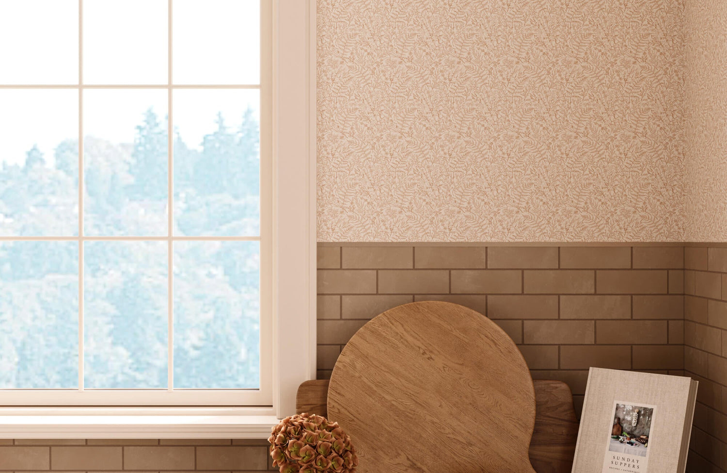 Soft beige botanical wallpaper with delicate leaf linework sits above warm taupe subway tile wainscoting, framed by a bright window and styled with layered wood accents.