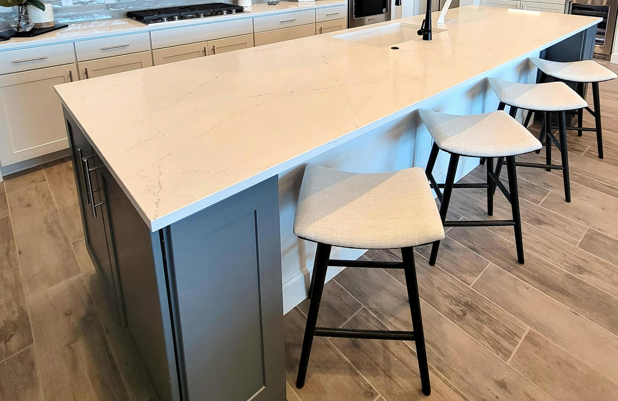 Modern kitchen featuring a large island with a quartz countertop, gray cabinetry, and wood look tile flooring in a warm natural tone.
