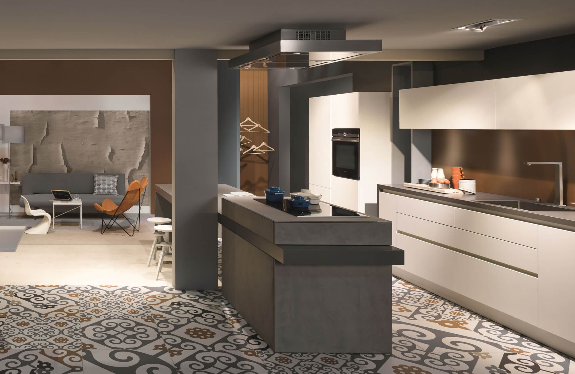 Modern kitchen design showcasing a sculptural island with an integrated cooktop, sleek white handleless cabinetry, a statement range hood, and patterned tile flooring that seamlessly connects the kitchen to an open-plan living area.