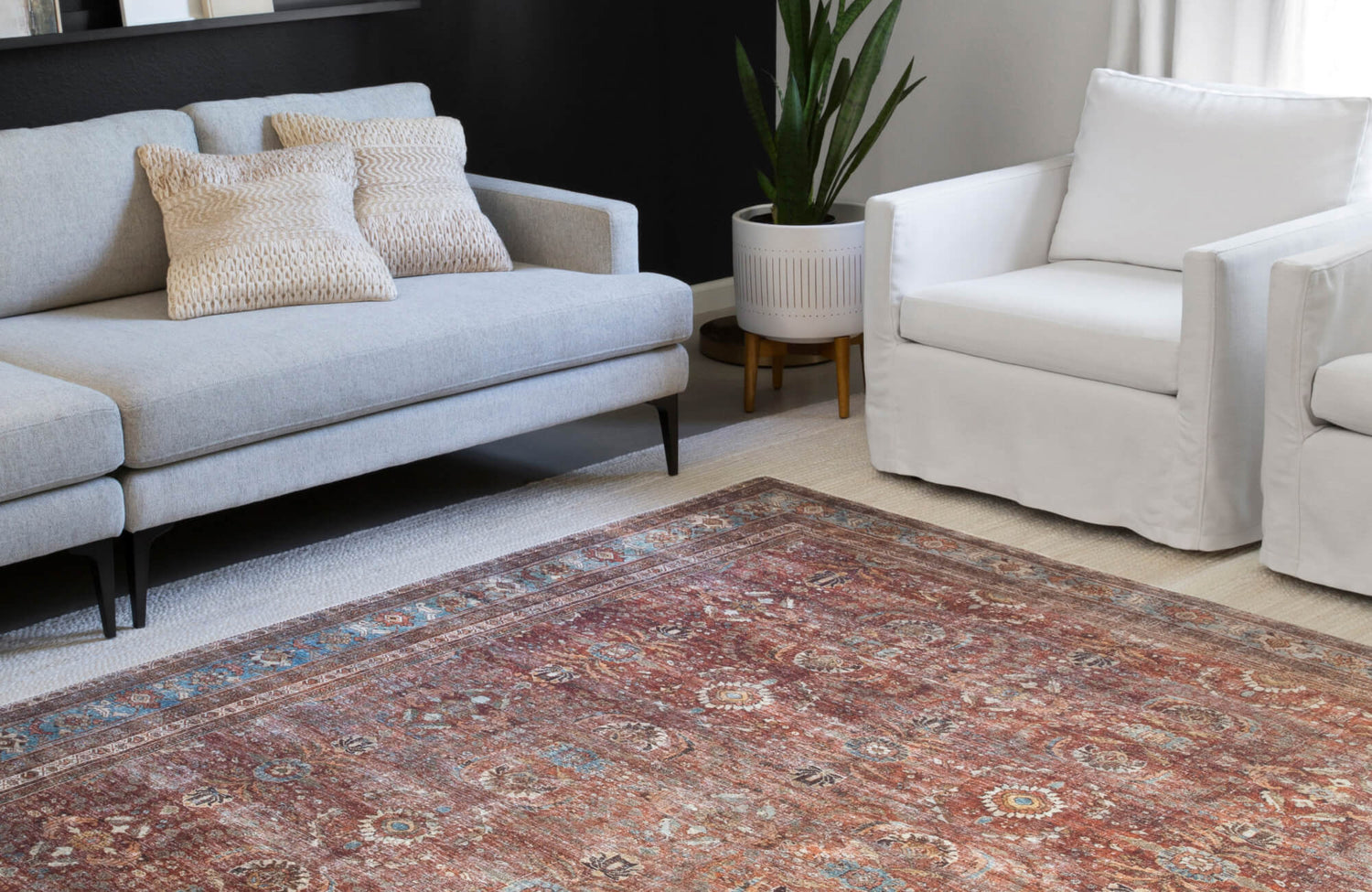 Living room with light grey sofa, white accent chair, vintage red and blue area rug, indoor plant, and layered neutral carpet