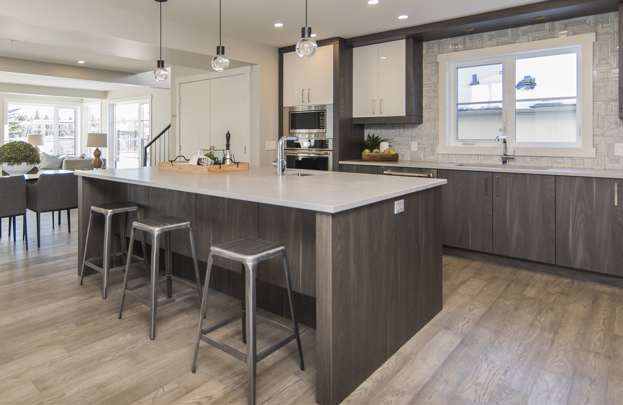 Modern open-concept kitchen with luxury vinyl plank flooring, featuring sleek gray cabinetry, a spacious island, and illuminated by recessed ceiling lights and black pendant fixtures with exposed bulbs.