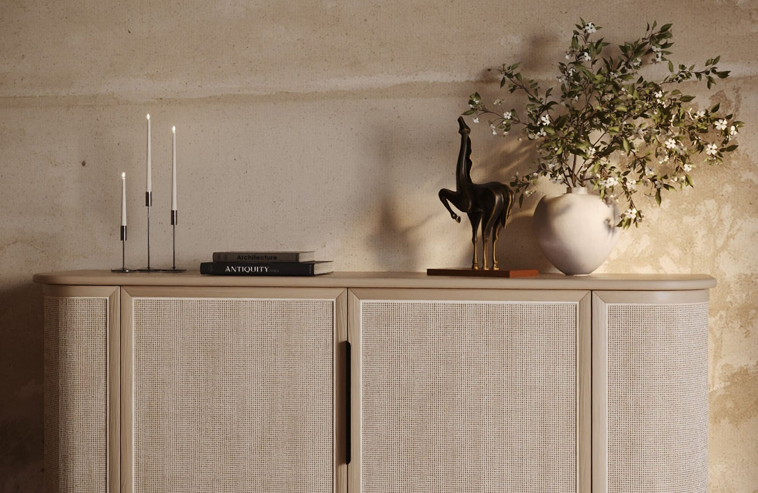 Modern horse sculpture styled on a light woven sideboard in a warm modern living room with candles, books, and a white vase.