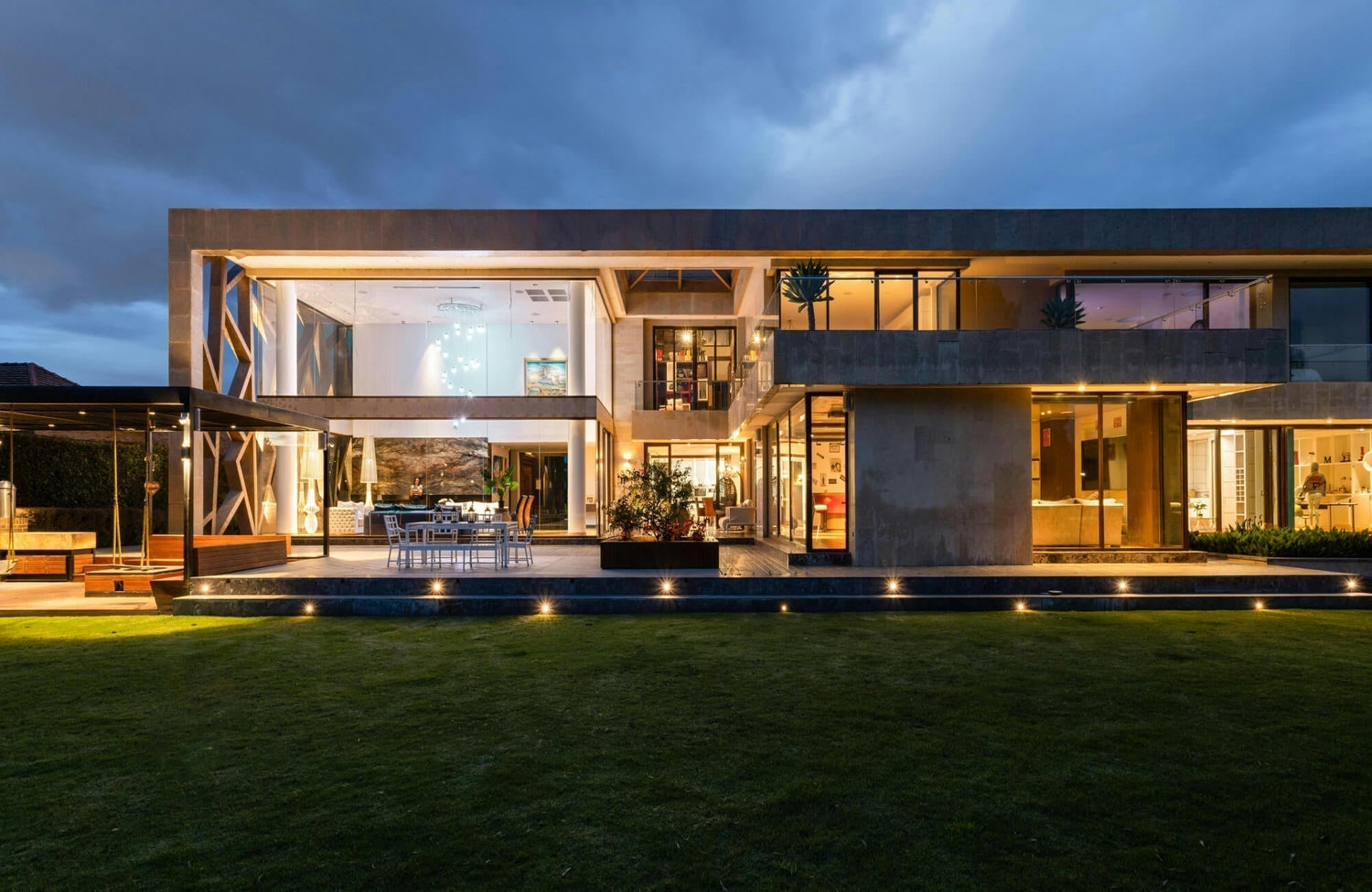 Modern outdoor house lighting with recessed step lights and warm architectural uplighting illuminates a modern glass-walled home, emphasizing clean lines and open terraces.