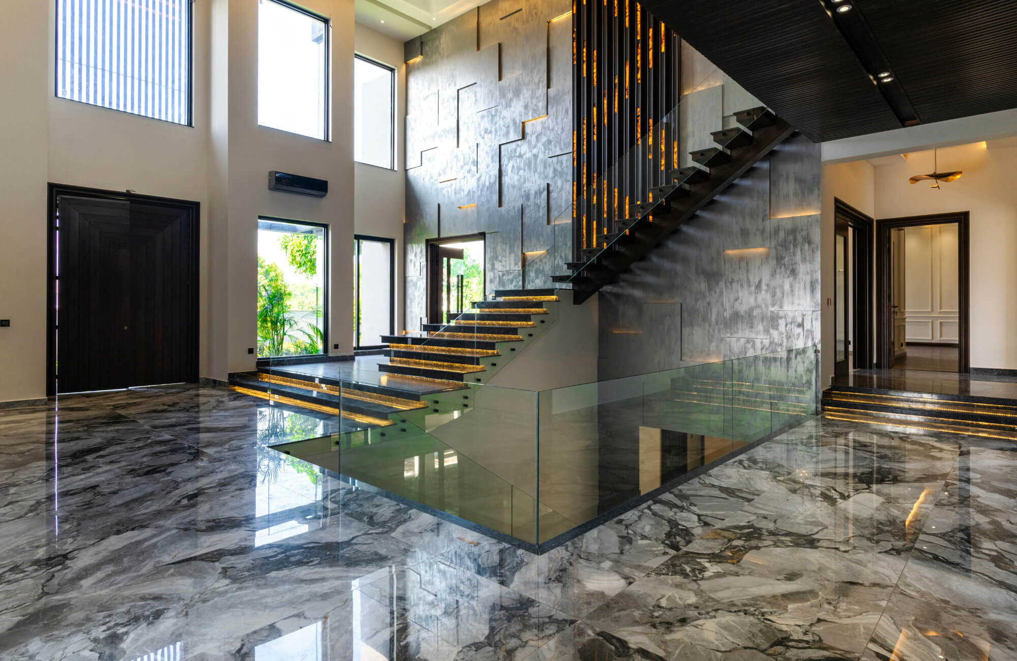 Luxurious modern interior featuring glossy marble-look tile flooring, dramatic staircase lighting, and floor-to-ceiling windows.