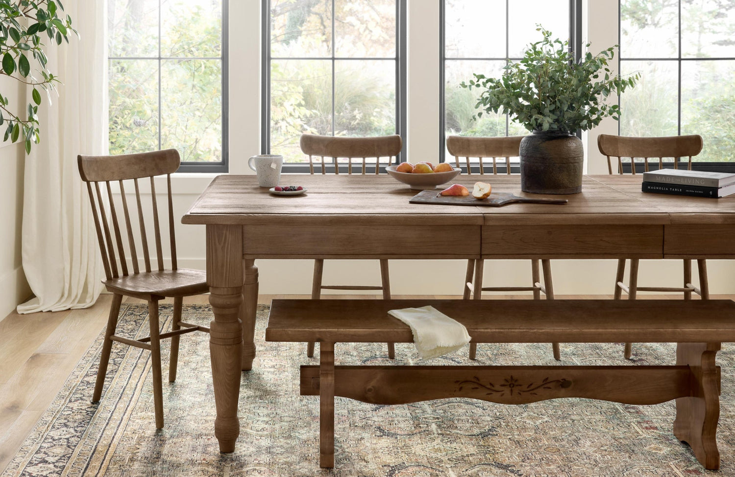 A traditional-style dining room with natural wood furniture and a light-toned patterned rug that brightens the space beneath the table.