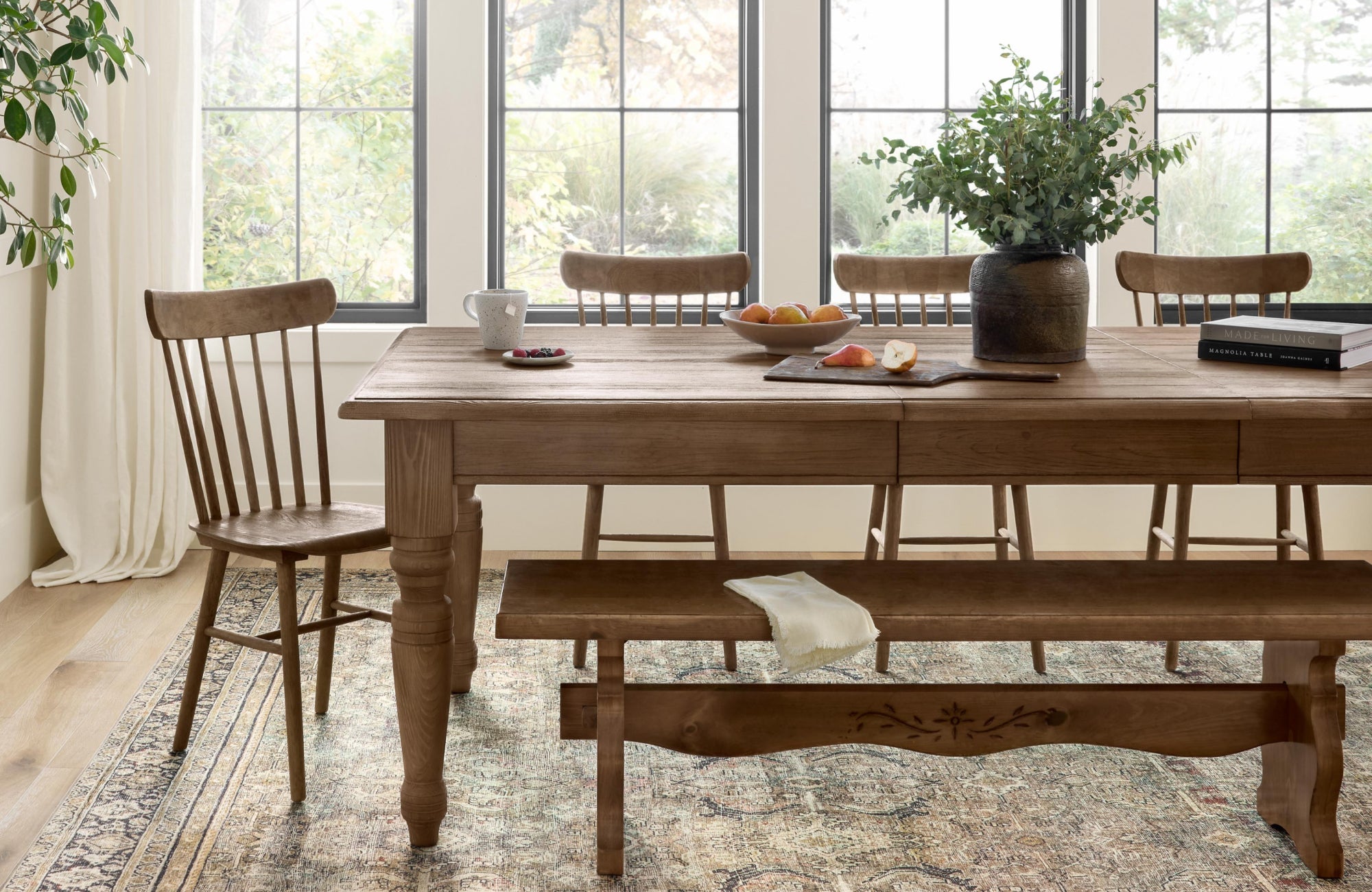 A traditional-style dining room with natural wood furniture and a light-toned patterned rug that brightens the space beneath the table.