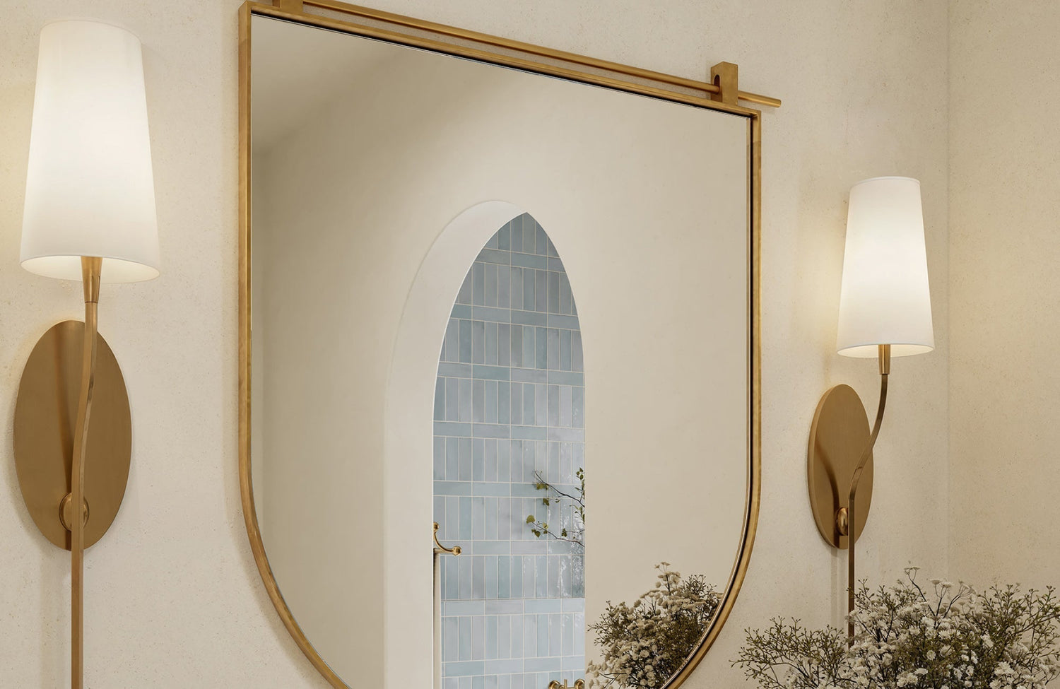 Gold wall sconces framing an arched mirror in a bright bathroom with light-toned walls and soft, elegant accents.