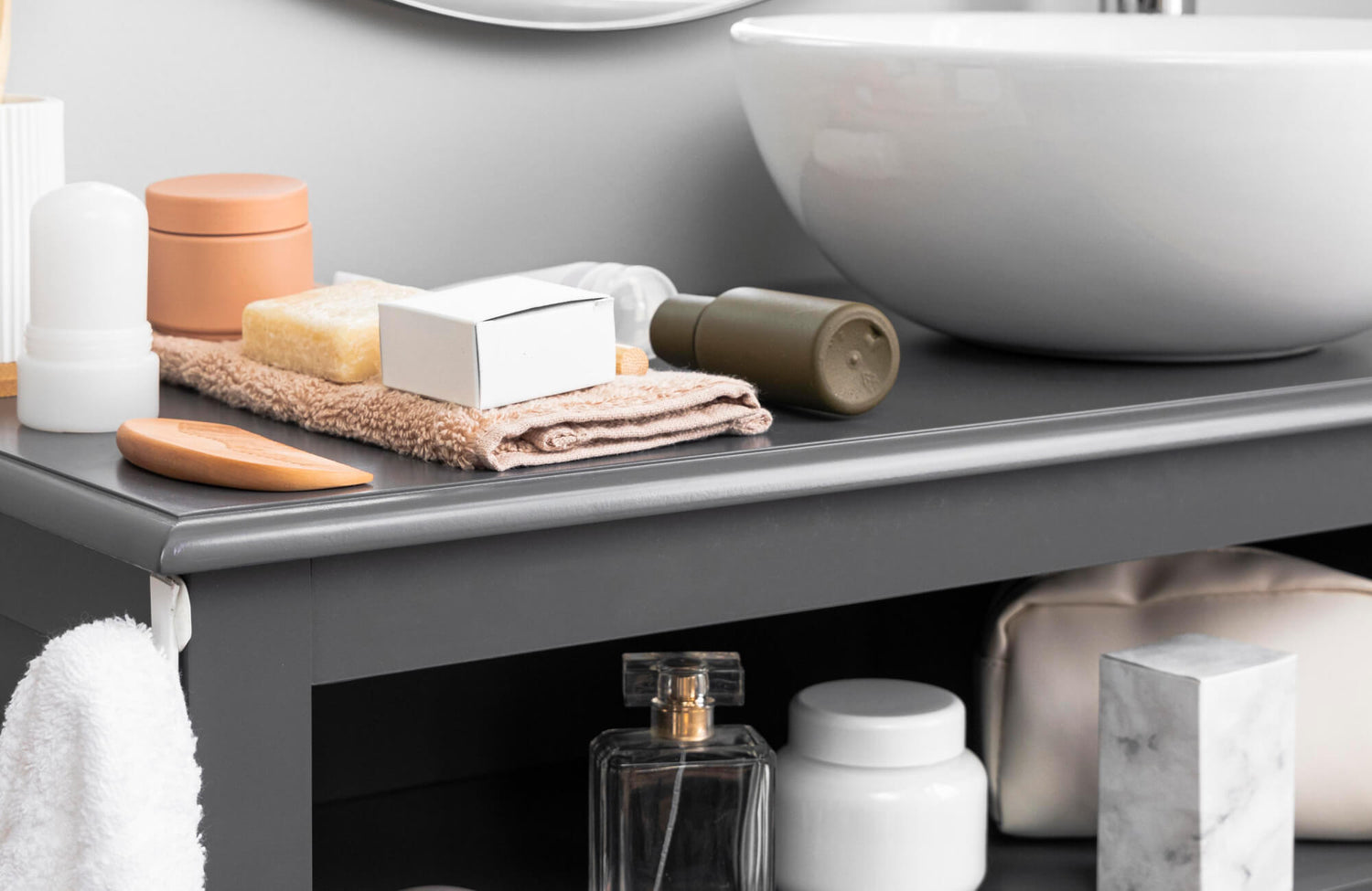 Modern bathroom vanity top with stacked neutral-toned towels, natural soap, and minimalist grooming essentials beside a white vessel sink.