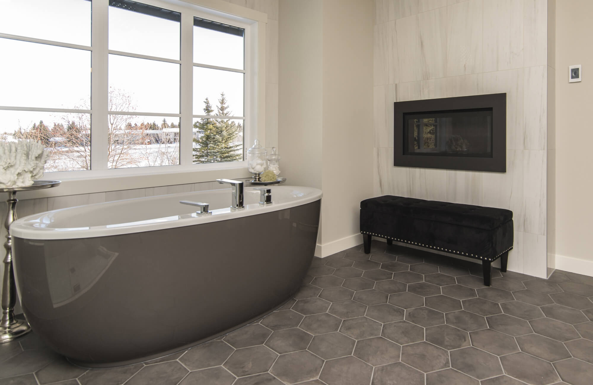 Luxurious bathroom with matte black hexagon tile flooring, complementing a sleek freestanding tub and modern fireplace feature wall.