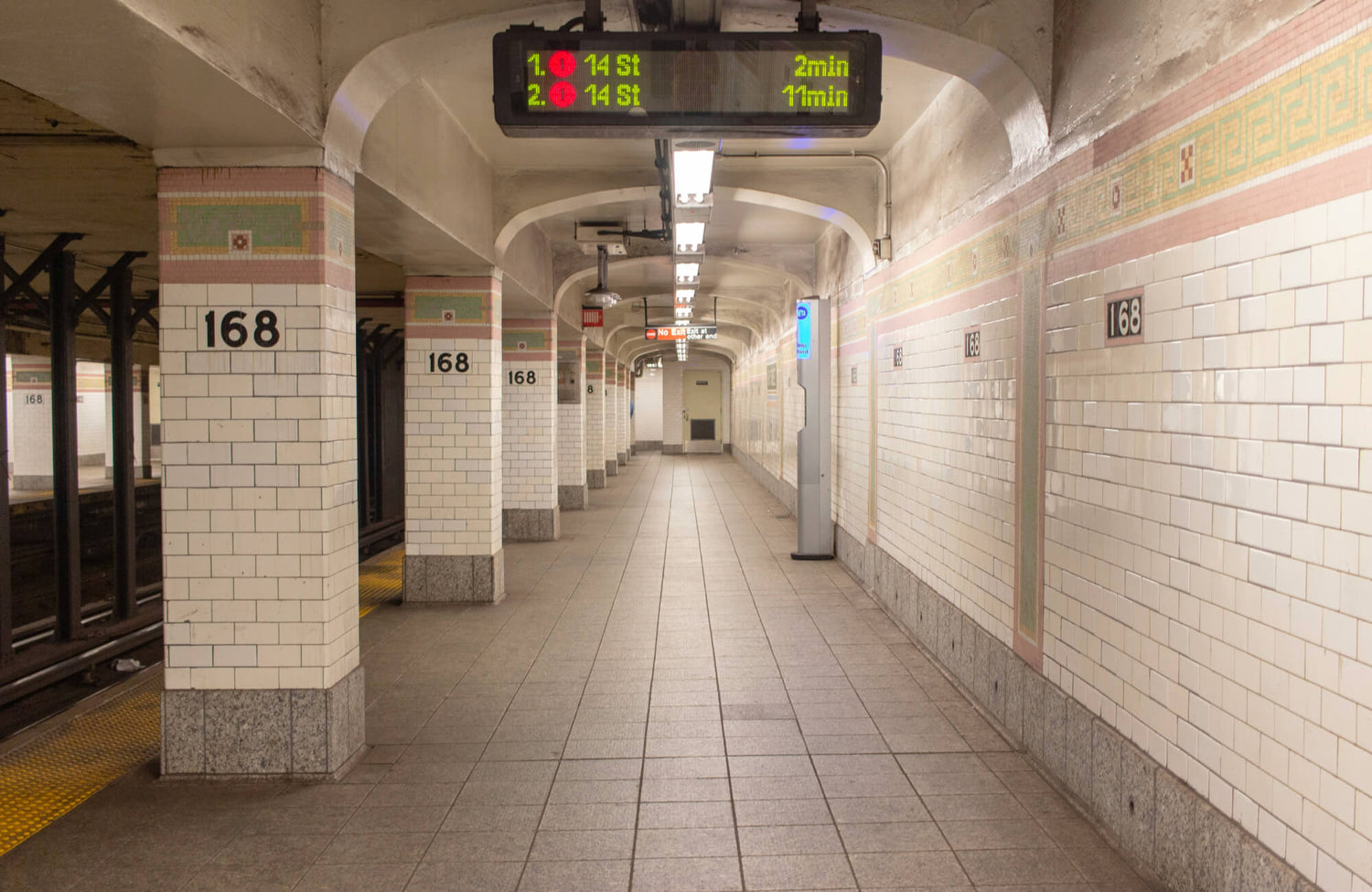 Historic New York City subway platform featuring classic white subway tiles with pink and green mosaic borders.