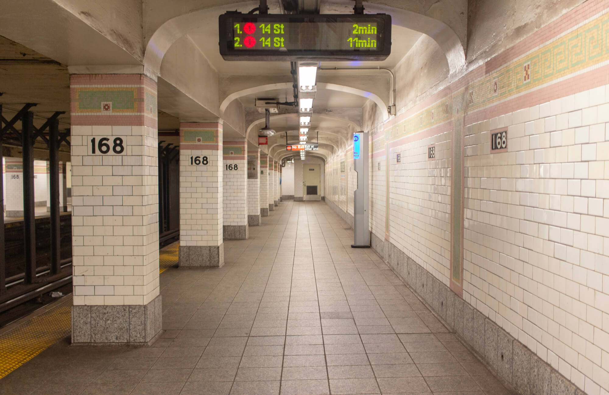 Historic New York City subway platform featuring classic white subway tiles with pink and green mosaic borders.
