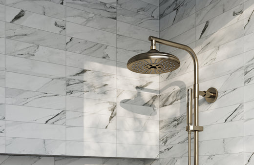 White marble-look shower wall tiles with gray veining in a modern bathroom, paired with brushed gold rain shower fixtures for a clean, luxury look.