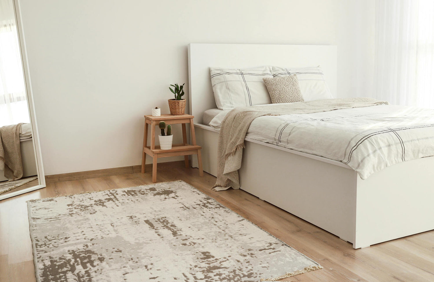 Cozy bedroom with a neutral-toned abstract area rug adding warmth and modern texture against light wood floors and minimalist white furniture.