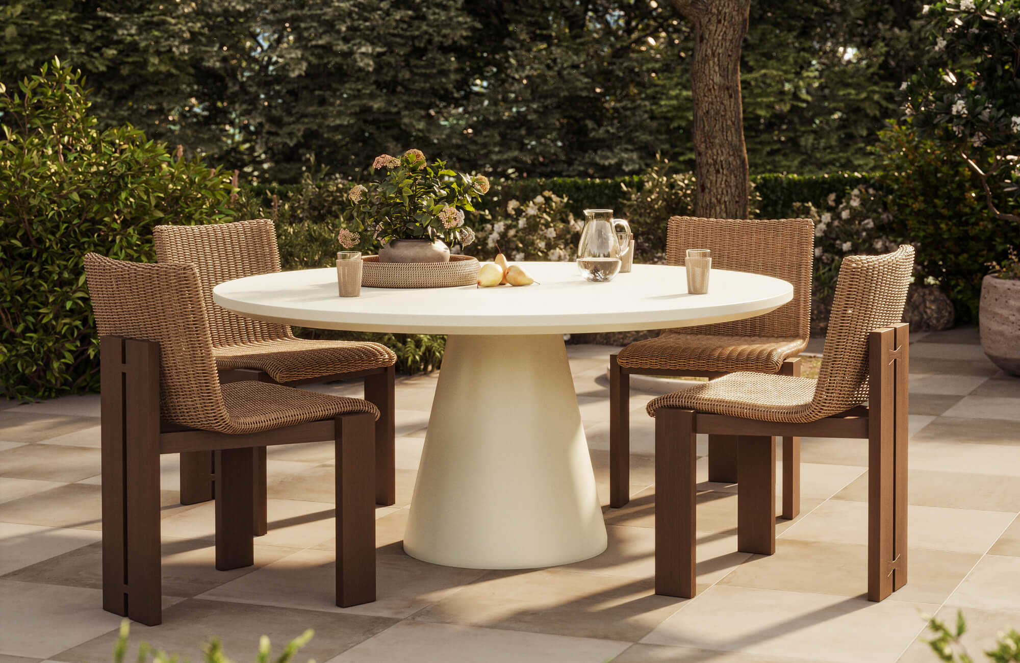 Outdoor patio dining set with woven chairs, a round pedestal table, and lush greenery in a warm garden setting.