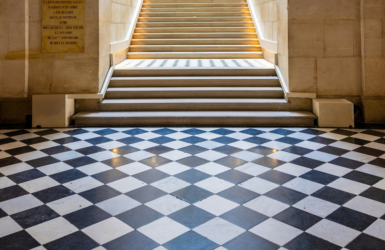 Elegant stone staircase with classic black-and-white diagonal checkerboard marble tile flooring in a grand architectural interior.