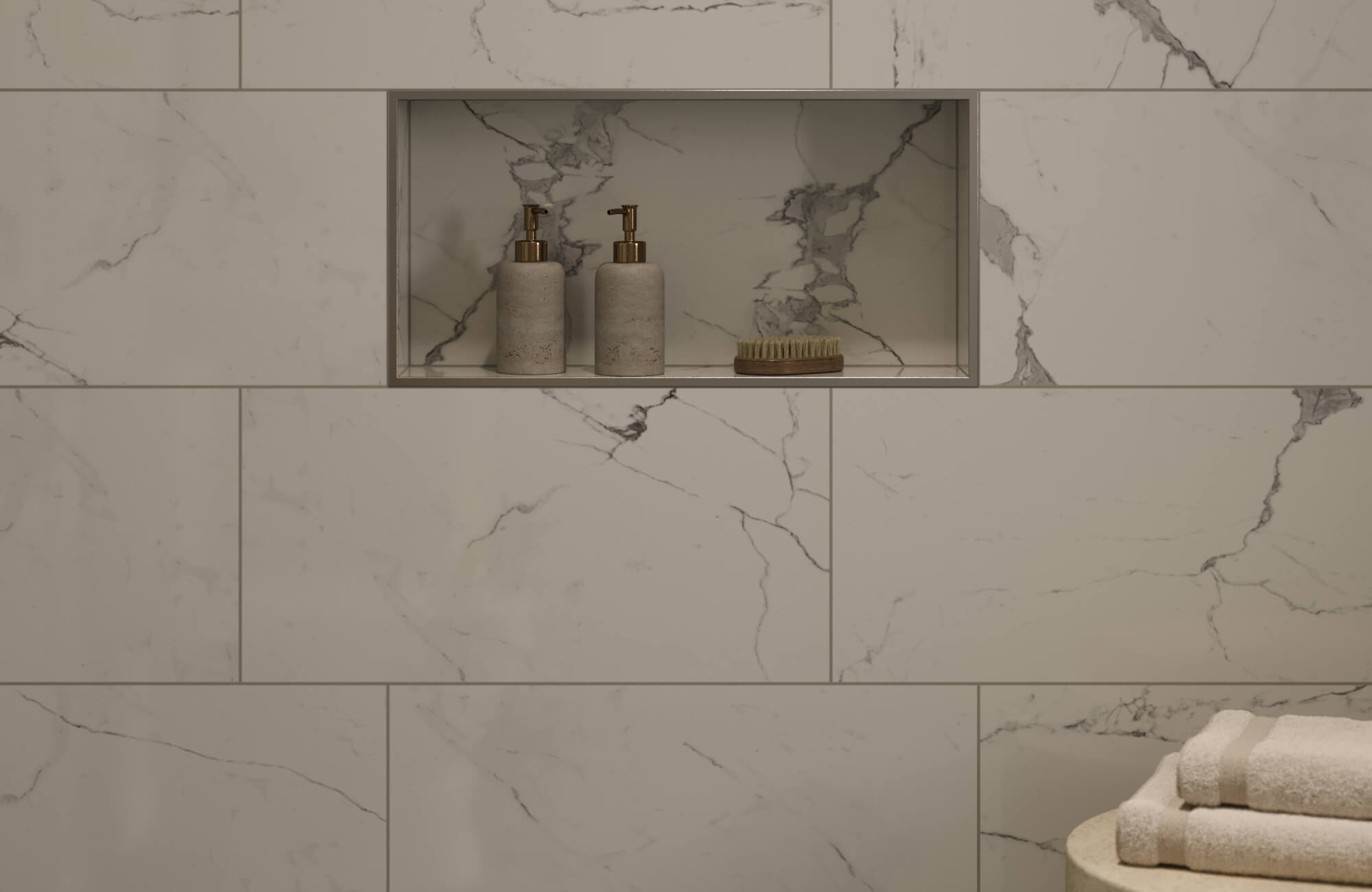 Shower wall clad in large-format marble-look tiles with subtle gray veining, featuring a recessed niche styled with bath essentials for a clean, modern aesthetic