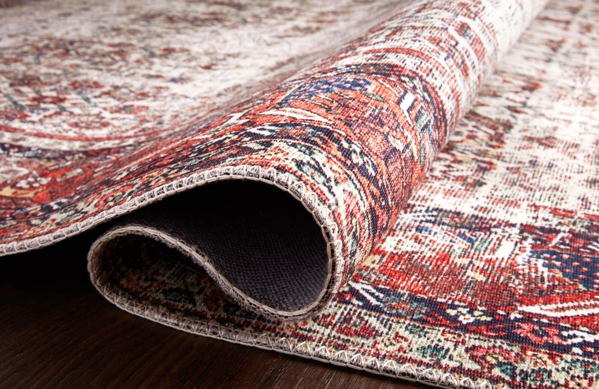 Close-up of a boho rug with warm red, blue, and cream tones showing detailed woven texture and soft vintage-style pattern.