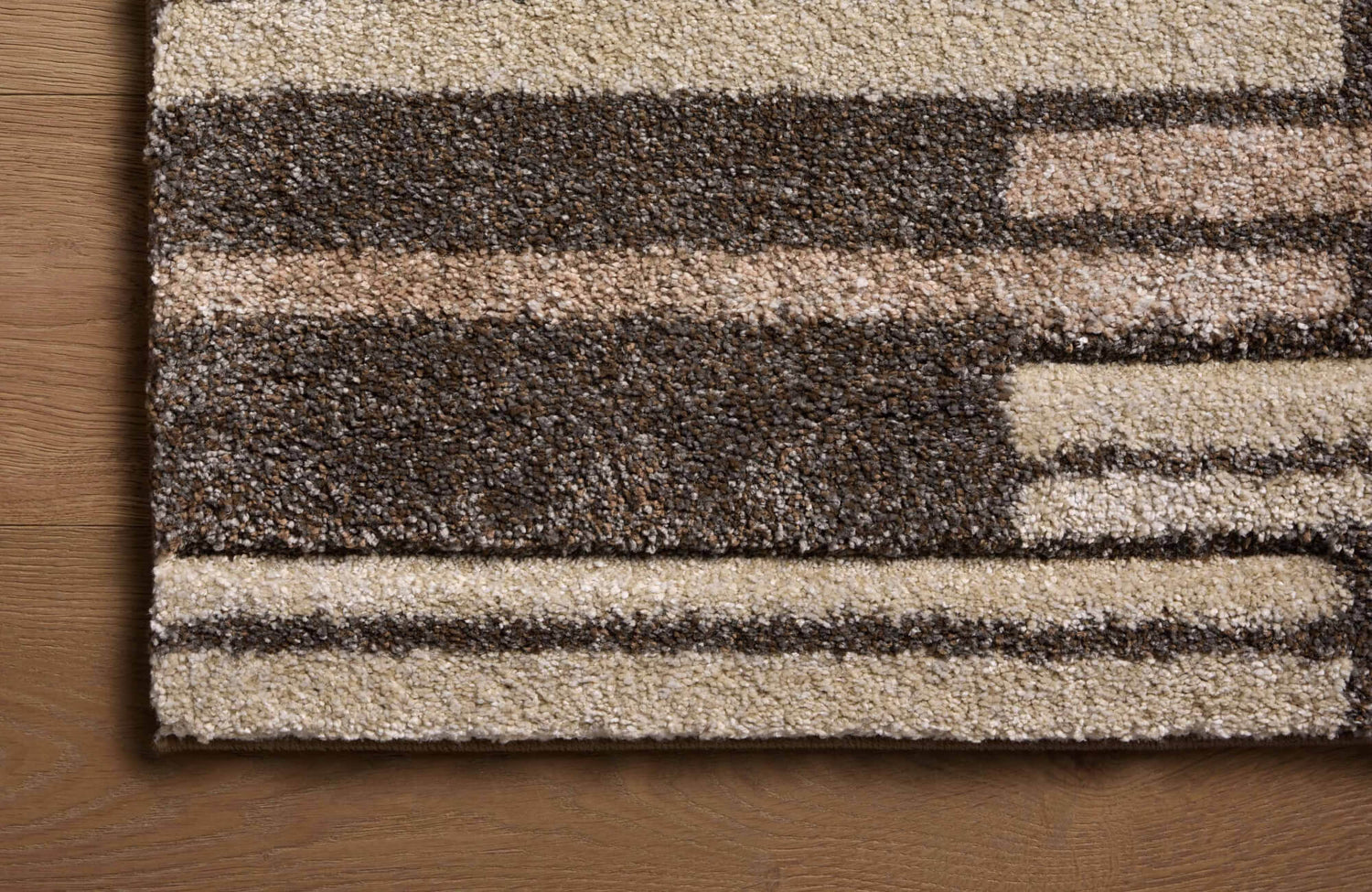 Close-up of a brown and beige polypropylene rug showing its dense texture against a light brown wood floor.