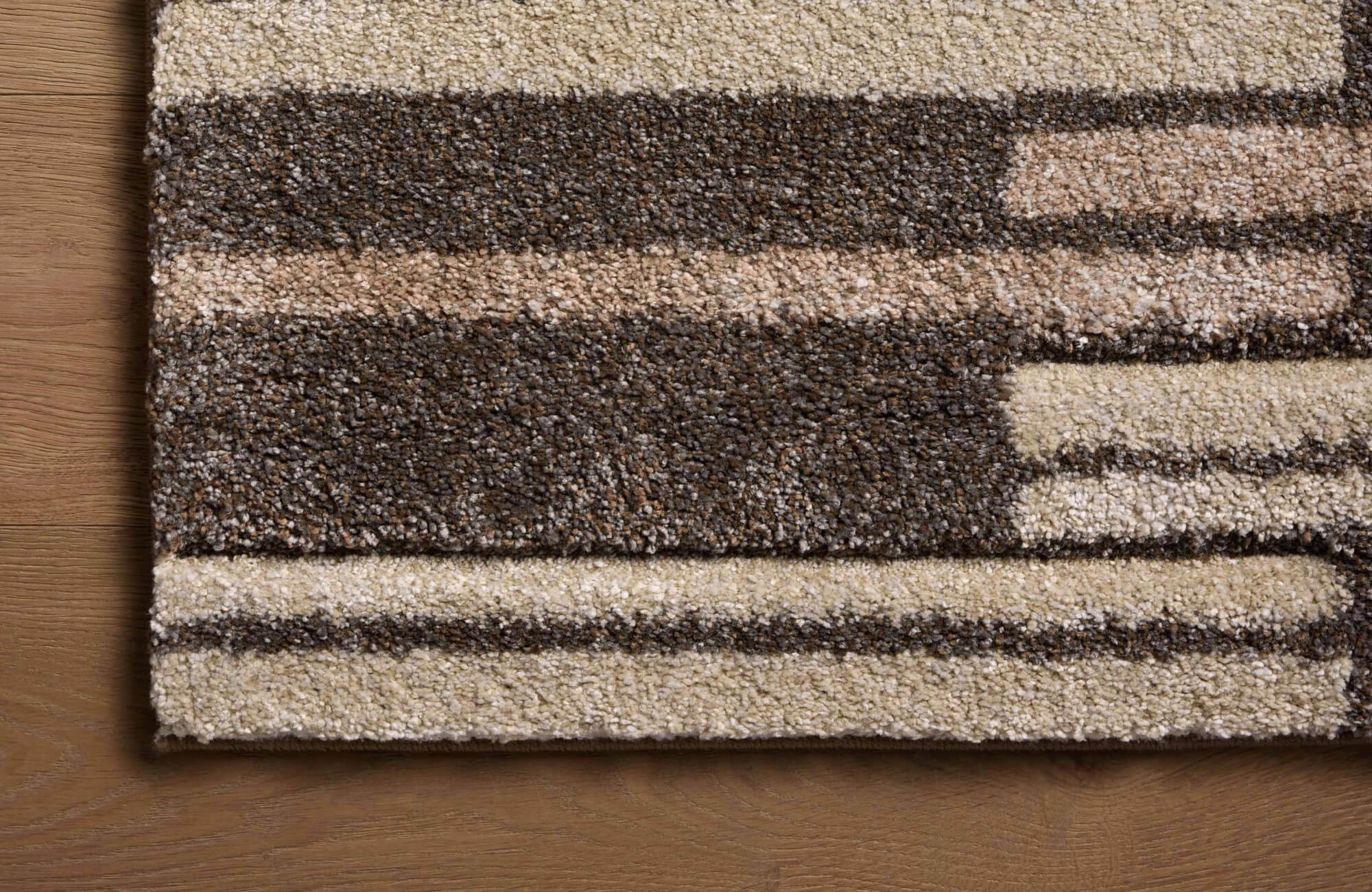 Close-up of a brown and beige polypropylene rug showing its dense texture against a light brown wood floor.