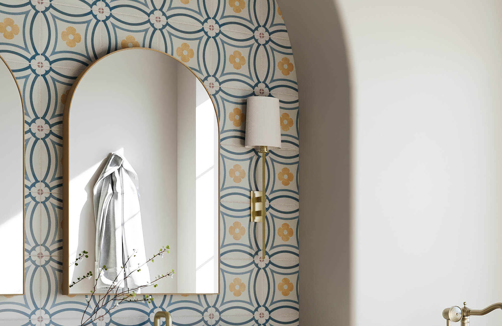 Arched mirror on floral patterned wall with brass sconce reflecting natural light and adding charm to this playful retro-inspired space