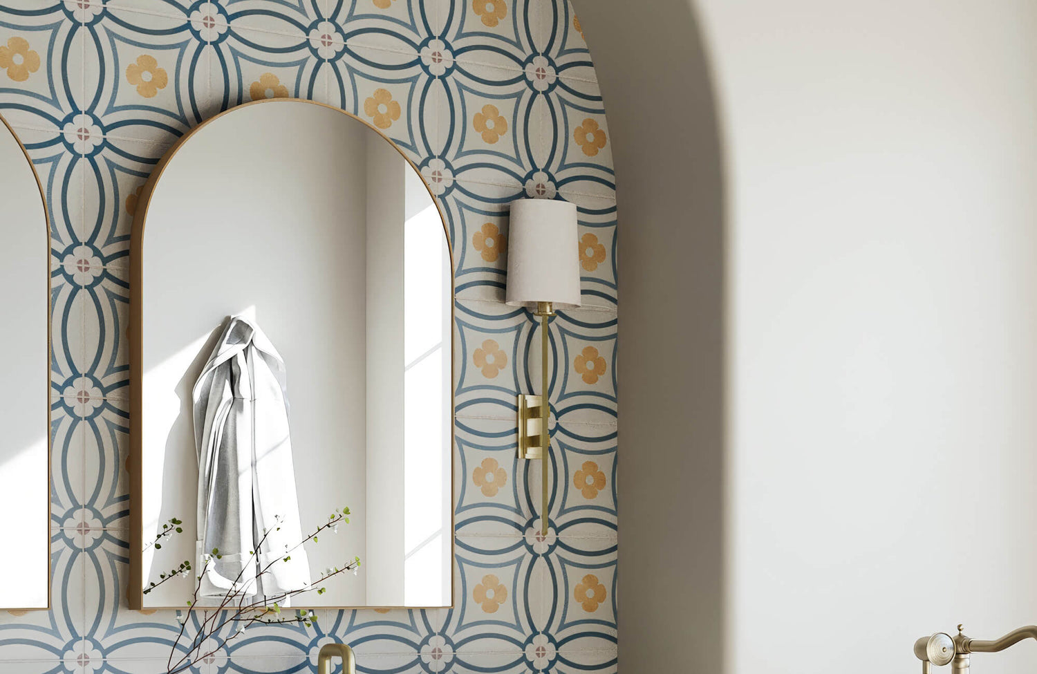 Arched mirror on floral patterned wall with brass sconce reflecting natural light and adding charm to this playful retro-inspired space