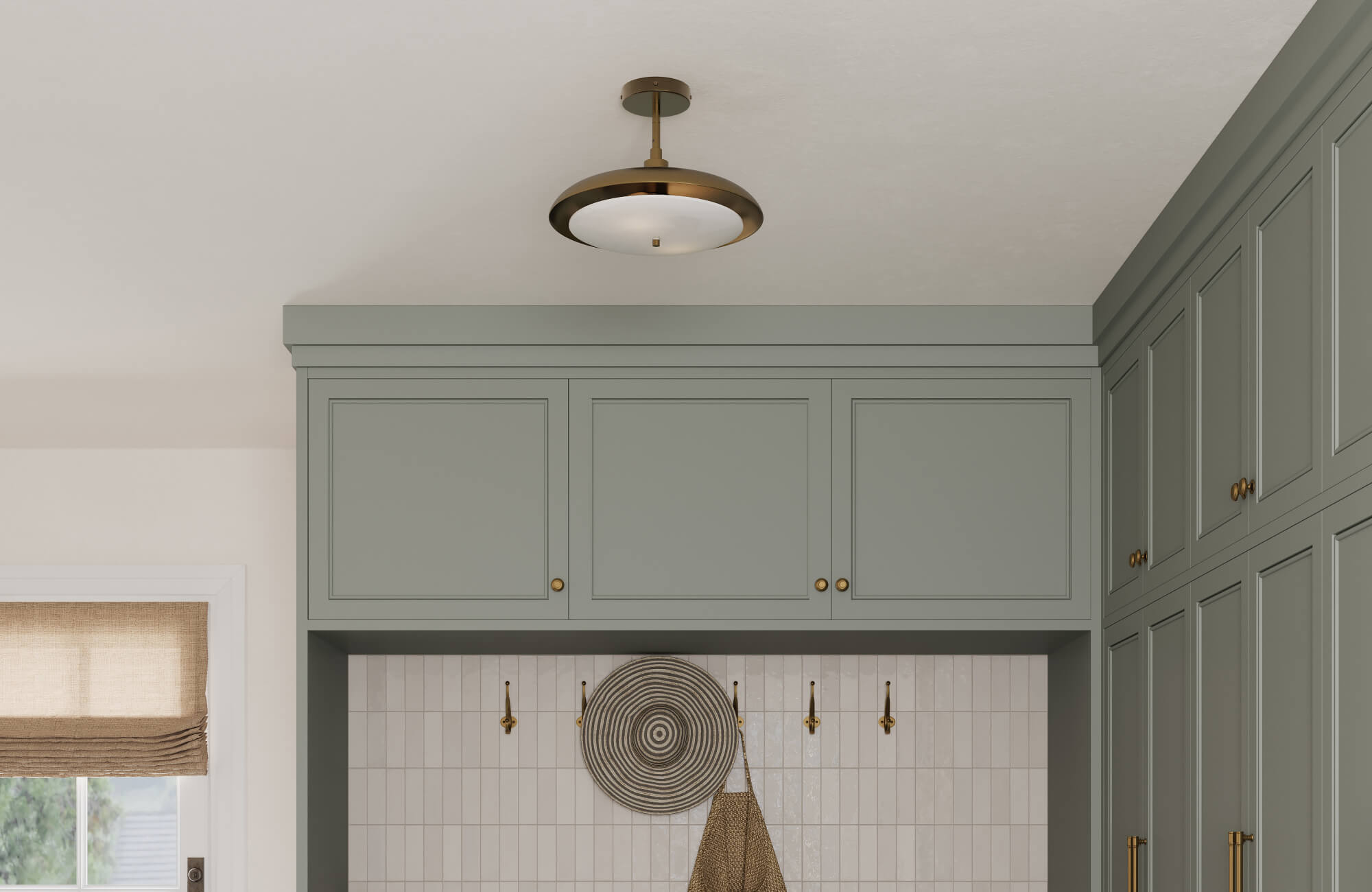 Soft green cabinetry with brass hardware and glossy white tiles is accented by a modern brass pendant light overhead.