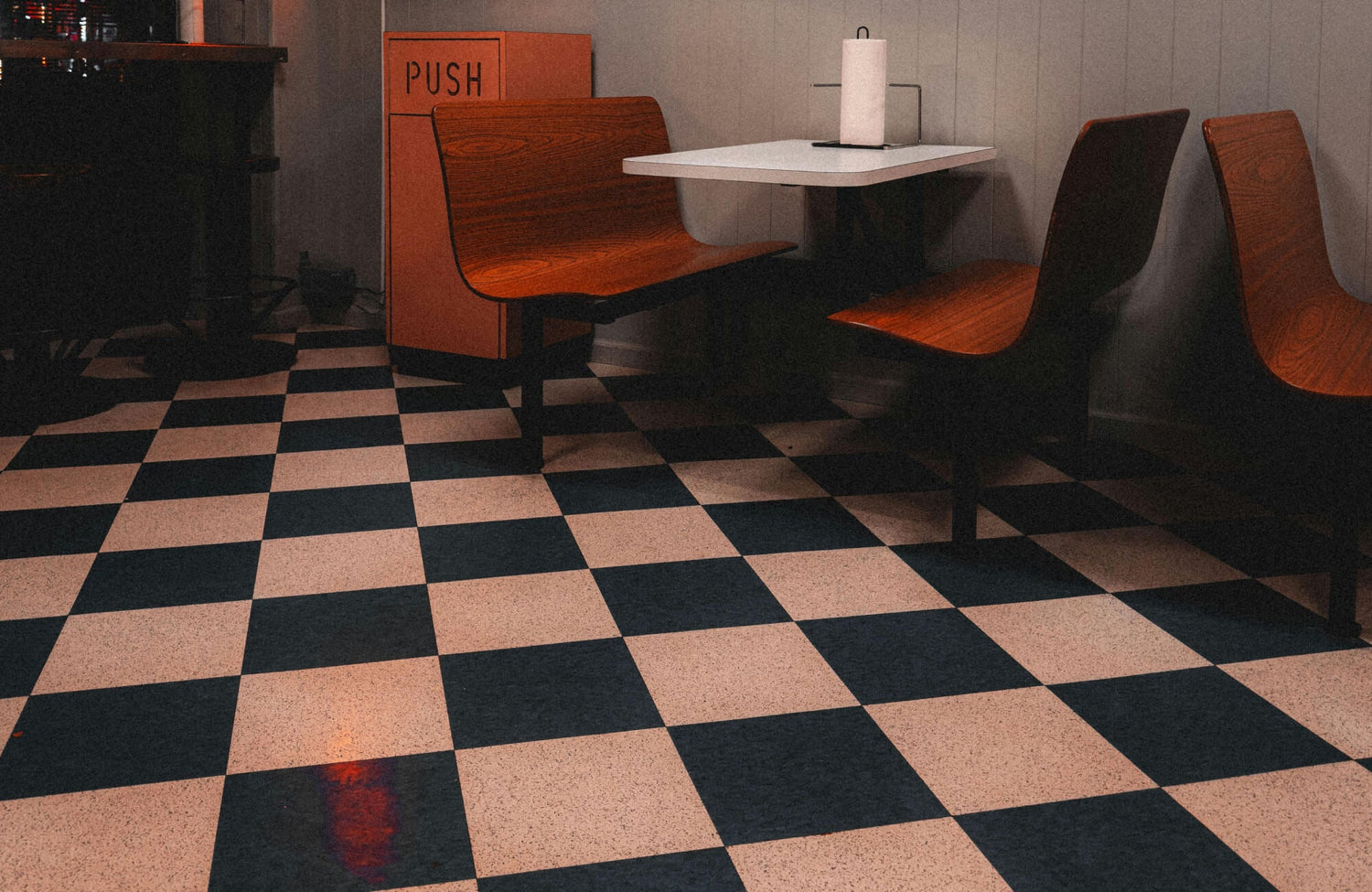 Classic black-and-white checkered tiles lend a retro diner vibe, perfectly complementing warm wood seating and vintage decor.
